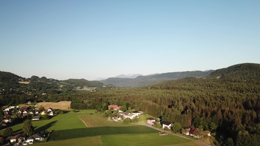 A drone capture of an Alpine ladscape in Austria. There are many small villages at the foothill of higher mountains. Lots of forest area. High mountain chains in the back. A vast lake in the back
