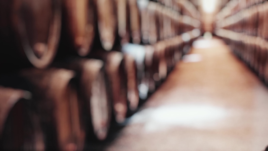 Two glasses of whiskey with ice are on a wooden table. In the background are barrels of whiskey.