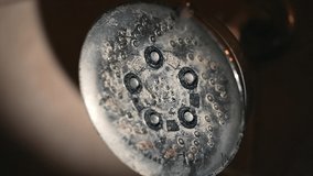 This close up, slow motion video shows a shower head faucet turning on as water begins to come out.