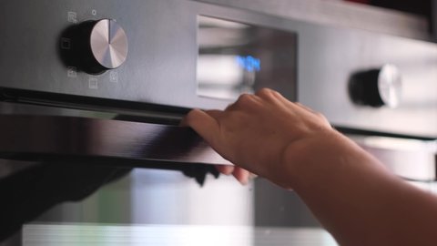 Close up of woman hand opening a modern cooking oven, kitchen utensils. Concept. Details of cooking process, putting a baking dish inside the oven.