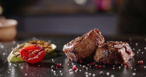 Chef decorating a plate with freshly grilled meat. Cooker adding a piece of rosemary with fingers on top of steak. Meal of grilled meat and vegetables - food art gourmet dinner 4k footage close up