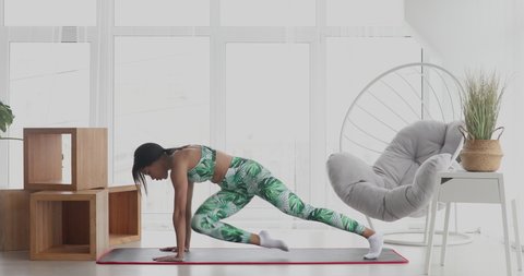 Young black woman making plank flexing legs exercise. Sporty fit girl doing fitness aerobic exercises. Home workout, training and wellness concept.