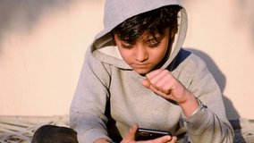 Portrait of Indian happy child boy wearing stylish hoodie and talking on videocall in mobile phone with vivid expression. Cute little vlogger Saying Hello, Hi looking at phone camera
