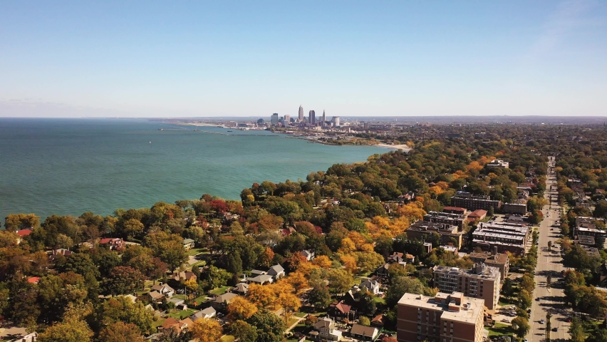 Beautiful aerial with a panoramic view of Cleveland, Ohio from a residential neighborhood flying towards the downtown skyline and water of Lake Erie on the horizon on a sunny blue sky autumn day. Royalty-Free Stock Footage #1064262181