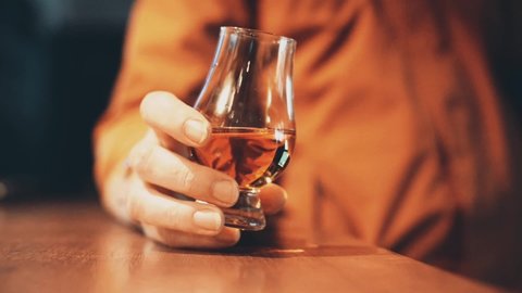 Color close up shot of a person holding a whisky glass on a wooden table, with shallow depth of field.