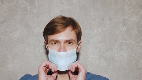 Handsome smiling hipster lumbersexual businessman model wearing casual jeans shirt clothes. Fashion stylish man posing against gray wall in studio. He putting on protective mask for corona virus
