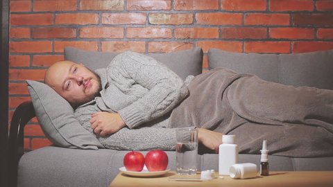 Diseased man lies on the sofa, coughing and drinks water, guy is sick and feels badly ill, infection coronavirus, covid-19 or flu illness