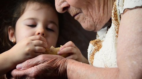 A small child feeds his grandmother with bread crumbs. The child feeds the old grandmother. The grandmother eats bread from the hands of a small child. Social advertising of poverty and hunger.