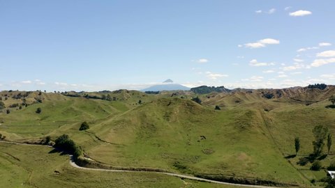 Volcano view over small grassy hills -  dramatic drone aerial footage with Lord of the Rings scenery - Mount Taranaki, Egmont National Park, New Zealand in 4k