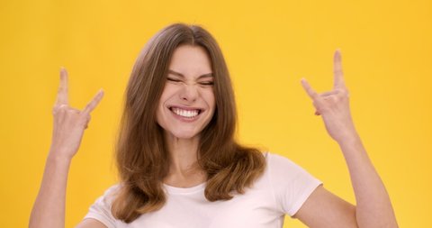 Rock-n-roll forever. Studio shot of young cheerful woman showing punk horn gesture, orange background, slow motion