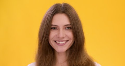 Cute playful woman winking to camera, flirting with you, yellow studio background, close up