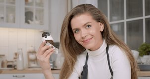 Close up portrait of young beautiful woman confectioner posing with selfmade decorated cupcake, smiling at camera at kitchen