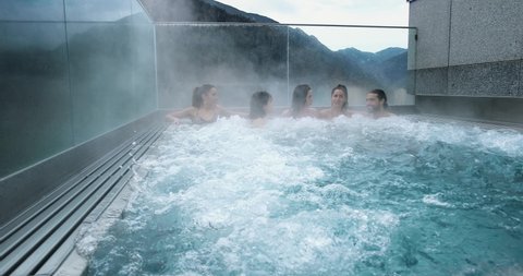 Outdoor jacuzzi with friends relaxing and having fun. We can see mountains in the background, perfect leisure activity in winter holidays 4K