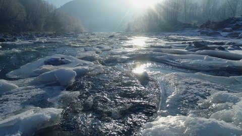 Mountain river with ice islands. Ice melts into a fast, seething river. Winter landscape with river, ice and trees