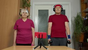 Mature couple man and woman fitness trainer coach records video online workout course with a smartphone live streaming sport exercises at home. Senior grandmother and grandfather live stream, blog