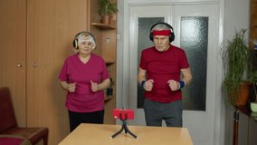 Senior elderly joggers couple man and woman watching online workout exercises on mobile phone and training, running together at home. Mature grandmother and grandfather during coronavirus lockdown