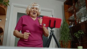 Senior elderly woman exercising, running. Old mature grandmother jogger doing workout with dumbbells, training, fitness, sport activity at home. Trainer shoots video blog trainings online vlog course