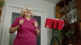 Senior elderly woman exercising. Old grandmother doing workout with dumbbells, training, fitness, sport activity at home. Trainer shoots video blog trainings online vlog course during coronavirus