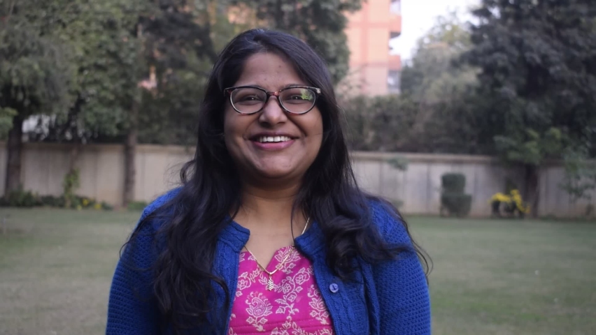 Indian girl with Spectacles smiling and laughing. She is standing in a garden and wearing winter clothing 