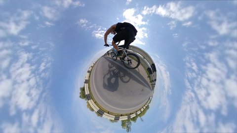 Bicycling. View of a small planet. 360 degree camera.
The cyclist rides fast on the road. Around the planet is the sky with clouds.