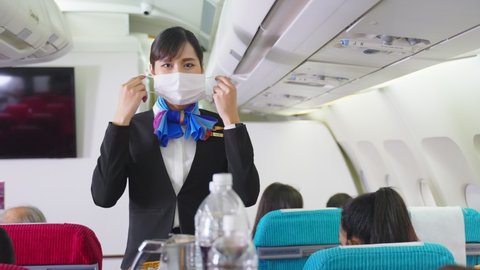 Cabin crew pushing service cart and serve to customer on the airplane during flight. New normal, flight attendant and all passengers wearing face mask to prevent COVID infection during virus pandemic.