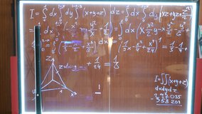 Hand written solved integral equation or mathematical formula on illuminated transparent glass marker board with LED-backlight on metal frame. Man silhouette shooting video on camera reflection