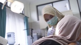 Female muslim dentist using medical mask on duty with her muslim patient. Wide shot of Asian hijabi dentist working on the hospital or healthcare HD. Conceptual video of healthcare service.