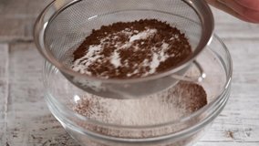 A Girl Hands Sifting Cocoa Powder and Flour Into Bowl On Table.