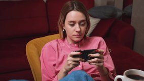  Young woman playing mobile game on cell phone at home. Attractive woman enjoying smartphone video games sitting on couch at living room.