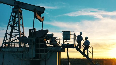 Two oil workers talking by an oil pump at sunset