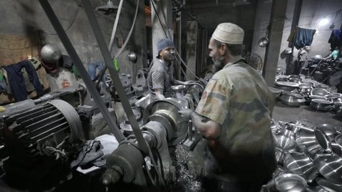 DHAKA, BANGLADESH - DECEMBER 20, 2020: Workers in an aluminium steel factory are polishing pots and pans in a dark sweatshop factory 