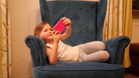 Little child girl lie in a chair takes smartphone selfie picture for own social media page