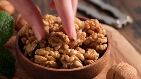 Walnuts in a wooden bowl. Healthy peeled nuts. Female hand picking a walnut
