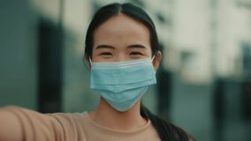 POV shot of Young Pretty Asian Woman in medical protective mask having a video call talking, waving hands and smiling chatting online communication with friend while standing outdoors in a city street