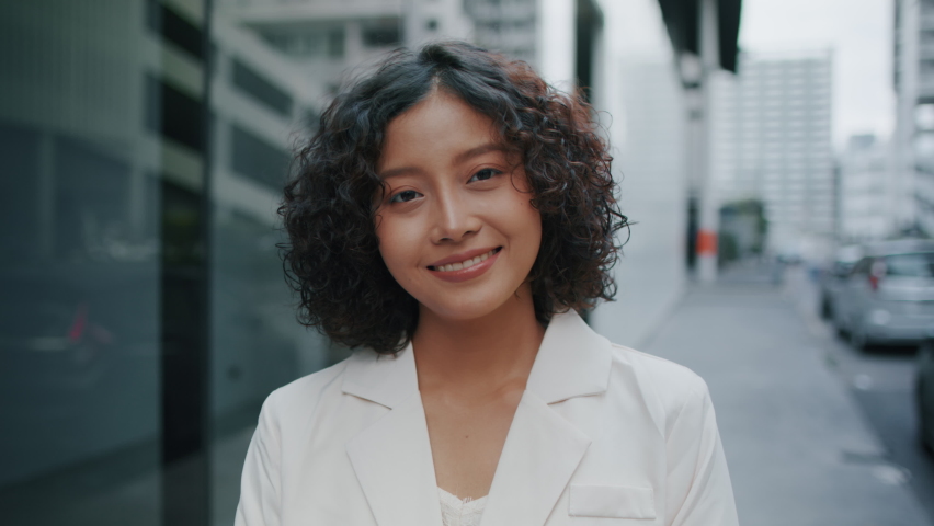 Young Attractive Indian Businesswoman Standing outdoor in street looking at camera and smiling. Portrait of Successful Businessperson smiling to camera standing in downtown with a confident expression | Shutterstock HD Video #1064355679