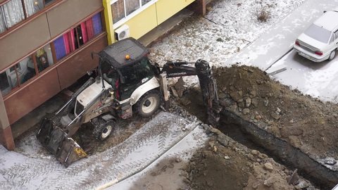Chelyabinsk, Chelyabinsk Region, Russia - december 05.2020: An excavator digs a trench in winter. The excavator is working next to a residential building. Excavator tracks in the snow. 