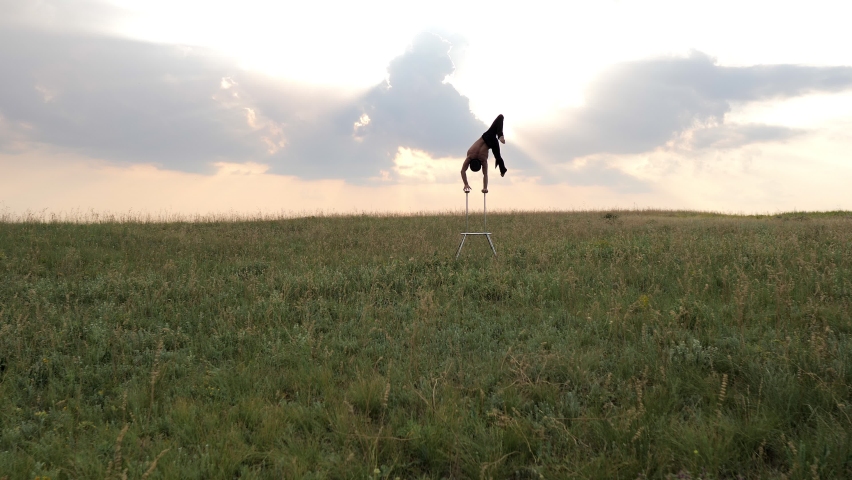 A man of athletic build performs complex gymnastic exercises in a field at sunset | Shutterstock HD Video #1064358622