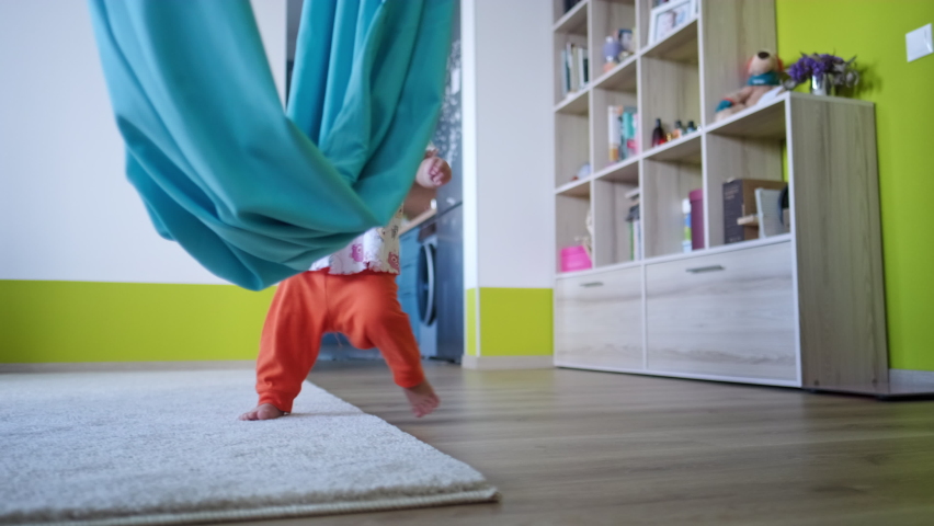 Toddler girl haves fun with hammock. Little todler girl plays and spins in the hammock in the bright and comfort living room