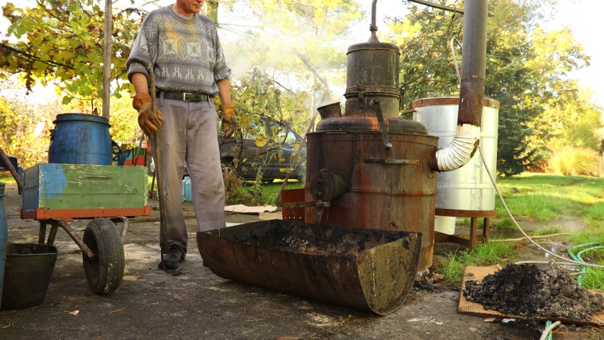Man is unloading boiler of homemade distillery made of copper to release used fruit marc, making moonshine schnapps, alcoholic beverages such as brandy, cognac, whiskey, bourbon, gin, and scotch.