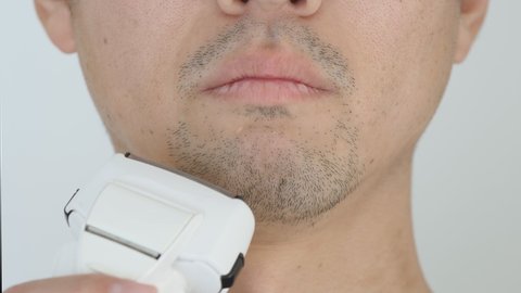 An adult man shave a slightly stretched black chin beard with an electric shaver. Asian men. Close-up. Isolated on white wallpaper background. Appearance grooming manner before going out. Lifestyle