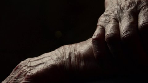 Old hands in the dark close-up. Wrinkles on the hands of an old grandmother close-up in the dark. Kind hands of grandmother close up. Old hands of a grandmother on a dark background. Old age concept