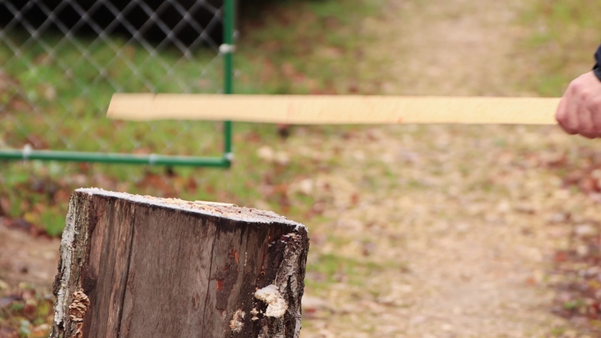 A man on a stump briskly chops a stick with an ax close-up. Preparing firewood for lighting the stove. The first snow fell. New year holiday is coming soon. Warm soft light.