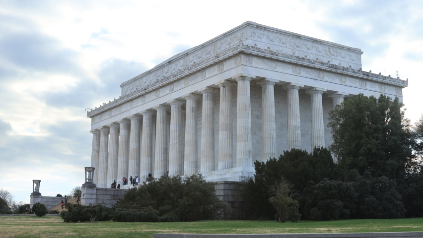 The east side of the Lincoln Memorial in Washington, D.C. Unidentifiable tourists walk up and down the steps. Cloudy skies on a late autumn day.