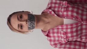 The young woman with her mouth taped writes that she can't. Woman with mouth tape with the message you can't do on white background. Message given silently.Video for the vertical story.