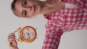 Young woman isolated on white background studio woman holding alarm clock and showing time. The woman looks at the watch and is angry. The concept of passing of time.Video for the vertical story.
