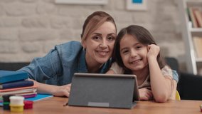 Family adult parents mother and little daughter having fun using digital tablet at home.Cute kid girl learning technology mother talking with kid look on pad screen at home.Smile looking at camera.