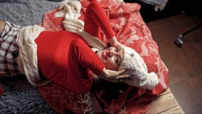 Pretty lady in white hat and scarf poses laying on bed. Christmas spirit video.