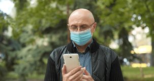 Bald senior man in medical protective mask communicates via smartphone. Covid concept health and safety, coronavirus quarantine, next wave covid virus protection. Cinema 4K 60fps video