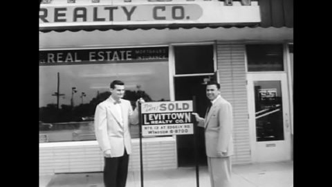 CIRCA 1950s - Real estate agents work in their office, and hammer a sold sign into a yard in Levittown, PA in 1954.