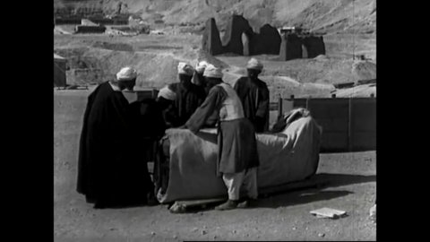 CIRCA 1920s - Egyptian laborers at an archeological site, Deir el Bahri, carefully pack ancient coffins into wooden crates to be shipped out.